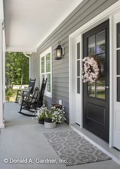 a porch with rocking chairs and flowers on the front door, along with an entrance rug