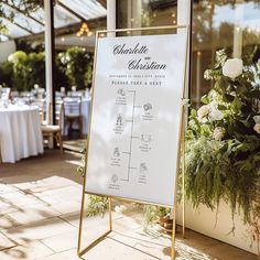 a sign that is sitting in front of a table with flowers and greenery on it