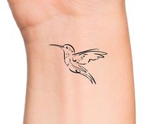 a small hummingbird tattoo on the left side of the arm, with black ink