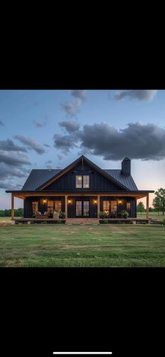 a large house with a covered porch in the middle of a grassy field at dusk