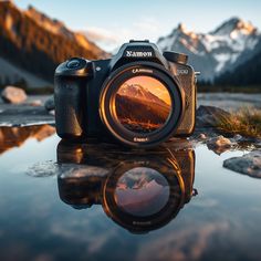 a camera sitting on top of a rock next to a body of water with mountains in the background