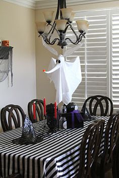 a dining room table decorated for halloween with black and white striped table cloths, ghost head hanging from the chandelier