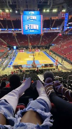 two people are sitting on the bleachers watching a basketball game in an arena