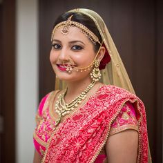 a woman in a red and gold bridal outfit with jewelry on her face, smiling at the camera