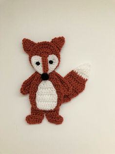 a crocheted red and white fox is shown on a white surface with one paw raised up