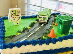 a birthday cake that is shaped like a road with trucks and traffic cones on it