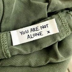 a label that says you are not alone on the back of a green shirt with white writing