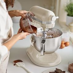 a woman mixing ingredients in a mixer on a kitchen counter with eggs and chocolates