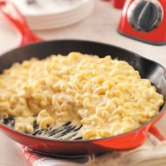 a red pan filled with macaroni and cheese on top of a white table