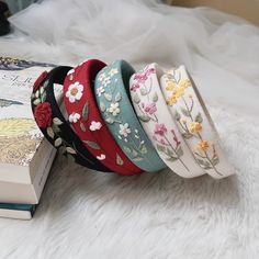 six headbands with flowers on them are sitting next to a book and white furnishing