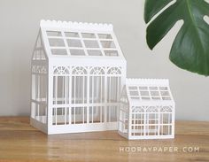 two white plastic model houses sitting on top of a wooden table next to a green plant