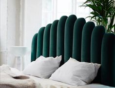 a bed with blue headboard and pillows in a room next to a potted plant