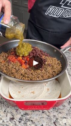 a person pouring something into a pan filled with food on top of a counter next to tortillas