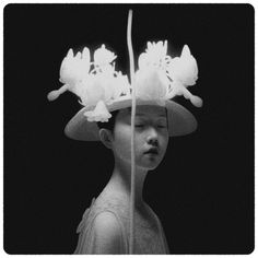 a black and white photo of a woman wearing a hat with flowers on her head