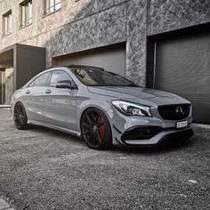 a silver mercedes cla parked in front of a building with two garage doors open