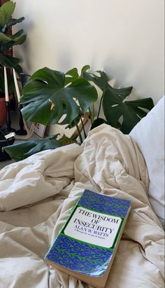 a book sitting on top of a bed next to a plant