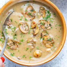 a person holding a spoon in a bowl of mushroom soup with parsley on top