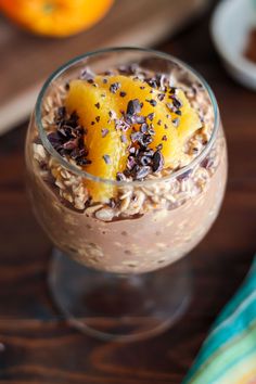 a dessert in a glass on top of a wooden table next to an orange slice