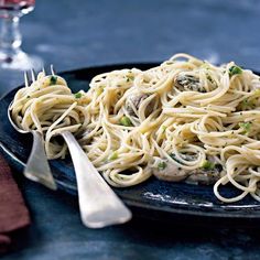 a black plate topped with pasta and meat next to a glass of wine on top of a table