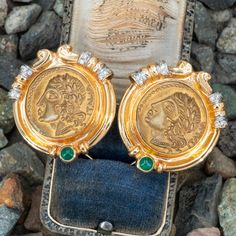 These Robert Bartholomew designed earrings are each centered with an Italian gold toned base metal token. The token depicts on the obverse with a Roman woman in profile wearing a leaf headdress, earrings and a beaded necklace . The reverse of the token depicts a soldier scene. The frame of the earrings are each accented with one (1), bezel set, round cabochon cut natural emerald and twelve (12), bead set, round brilliant cut diamonds. The earrings measure 31mm wide and is finished with omega style backs. Trademarks: RB 14K. There is a matching necklace for this earrings and the SKU number is A93764. Woman In Profile, Medallion Earrings, A Soldier, Bead Set, Matching Necklaces, Natural Emerald, Round Brilliant Cut Diamond, Modern Jewelry, Base Metal