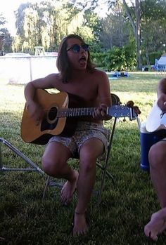 two people sitting in the grass playing guitar and singing to someone else who is holding a frisbee