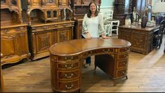 a woman standing next to a large wooden desk in a room filled with antique furniture