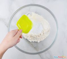 someone mixing ingredients in a glass bowl on a marble counter top with a yellow spatula