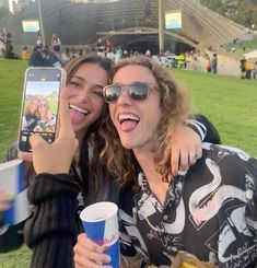 two people taking a selfie with their cell phone at a sporting event in the sun