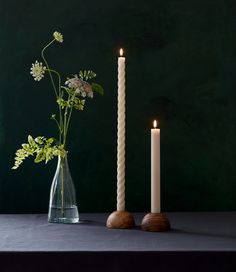 two white candles sitting on top of a table next to a vase filled with flowers