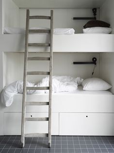 bunk beds with white linens and pillows in a small room next to a ladder