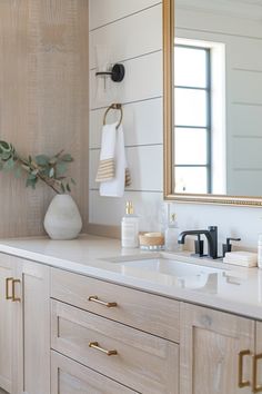 a bathroom vanity with white counter top and wooden cabinetry, gold pulls on the mirror