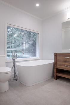 a white bath tub sitting next to a toilet in a bathroom under a large window