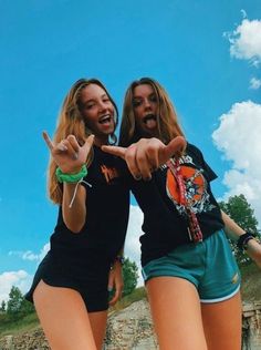 two young women pointing at something while standing next to each other in front of a blue sky