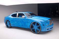 a blue car is parked in front of a gray wall with black wheels and rims