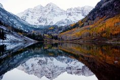 the mountains are covered in snow and fall colors as they reflect in the still water