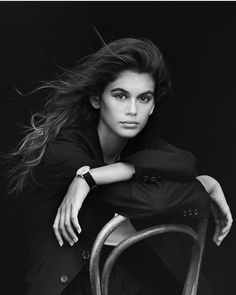 a black and white photo of a woman leaning on a chair with her hair blowing in the wind