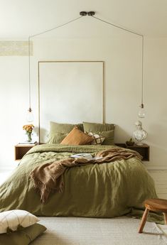 a bed with green linens and pillows in a white room, next to a wooden bench