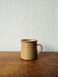 a brown mug sitting on top of a wooden table next to a white textured wall