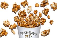 a bucket filled with caramel popcorn sitting on top of a white table next to nuts