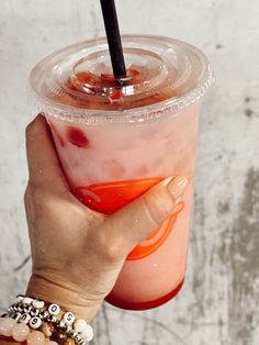 a person holding up a drink with a straw in it's hand and wearing bracelets