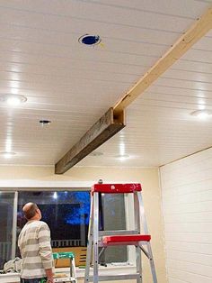 a man standing on a step ladder in front of a kitchen with wood beams attached to the ceiling