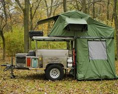 an off - road camper is set up in the woods with its roof open