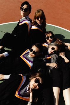 four young women laying on top of each other in front of a tennis ball court