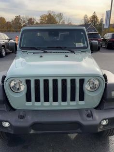 the front end of a light blue jeep parked in a parking lot with other cars