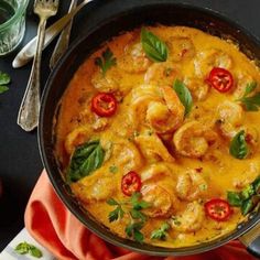 a skillet filled with shrimp and cheese on top of a red cloth next to silverware