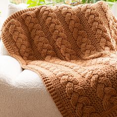 a brown knitted blanket sitting on top of a white couch next to a potted plant