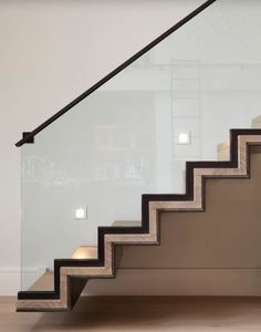 a stair case with glass handrails and black rails on the bottom, in front of a white wall