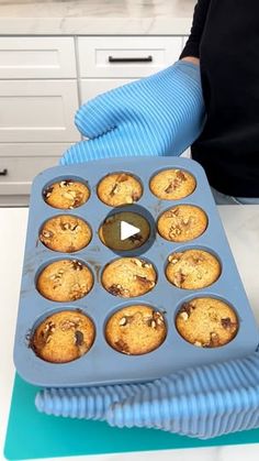 a person in blue gloves is holding a muffin tray