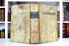 an old book sitting on top of a table next to bookshelves filled with books