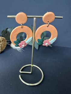 a pair of earrings with flowers and leaves on them, sitting on a metal stand